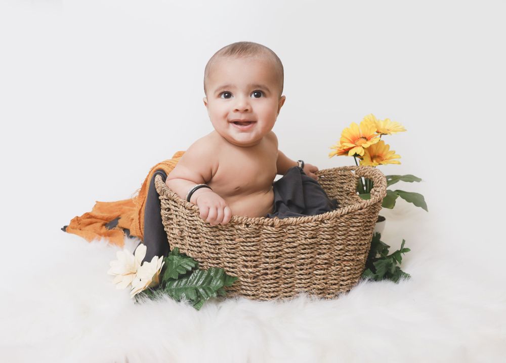 Baby sitting in wicker basket with sunflower and greenery on white background.