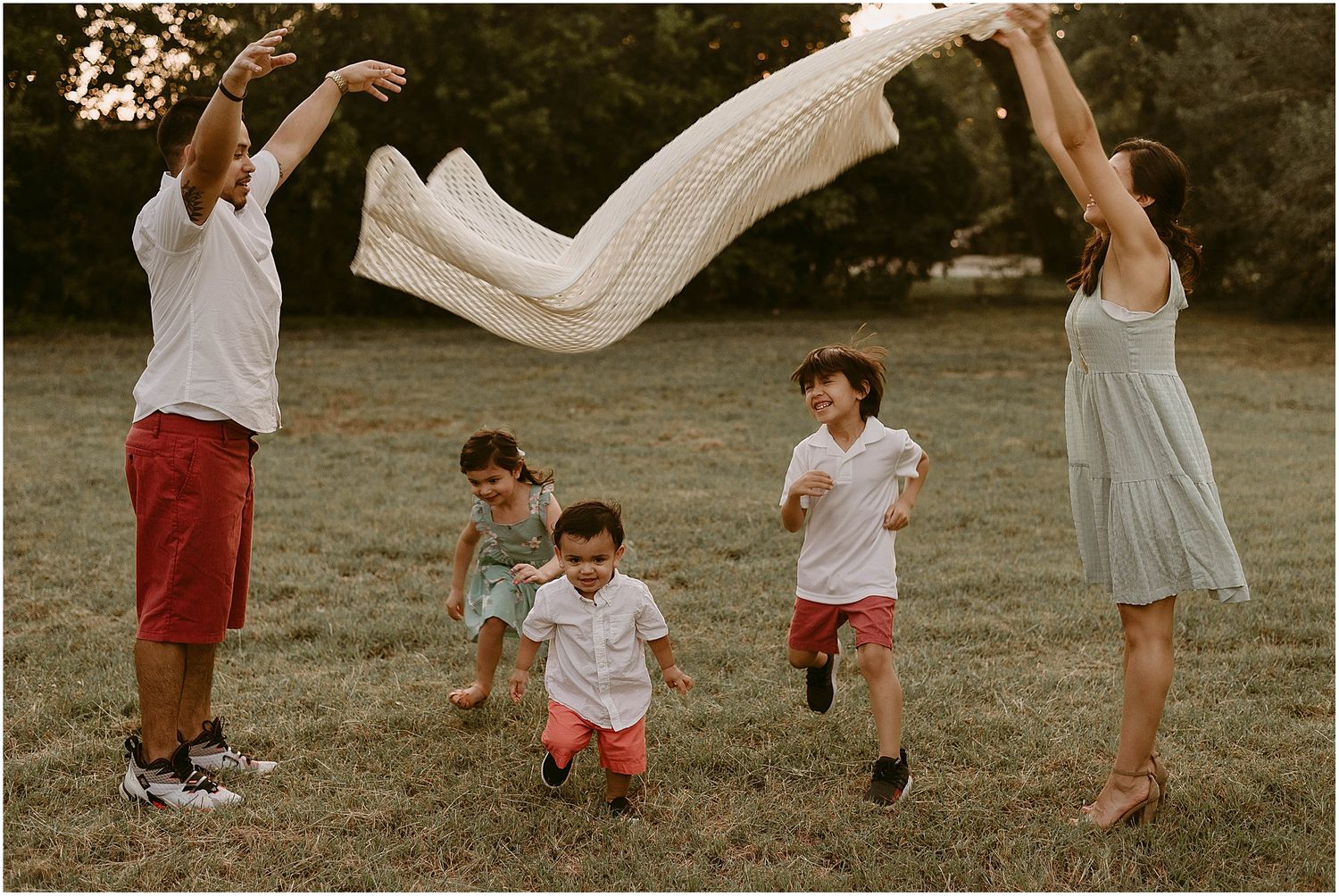 Family creates a canopy with white fabric while children run beneath during sunset.
