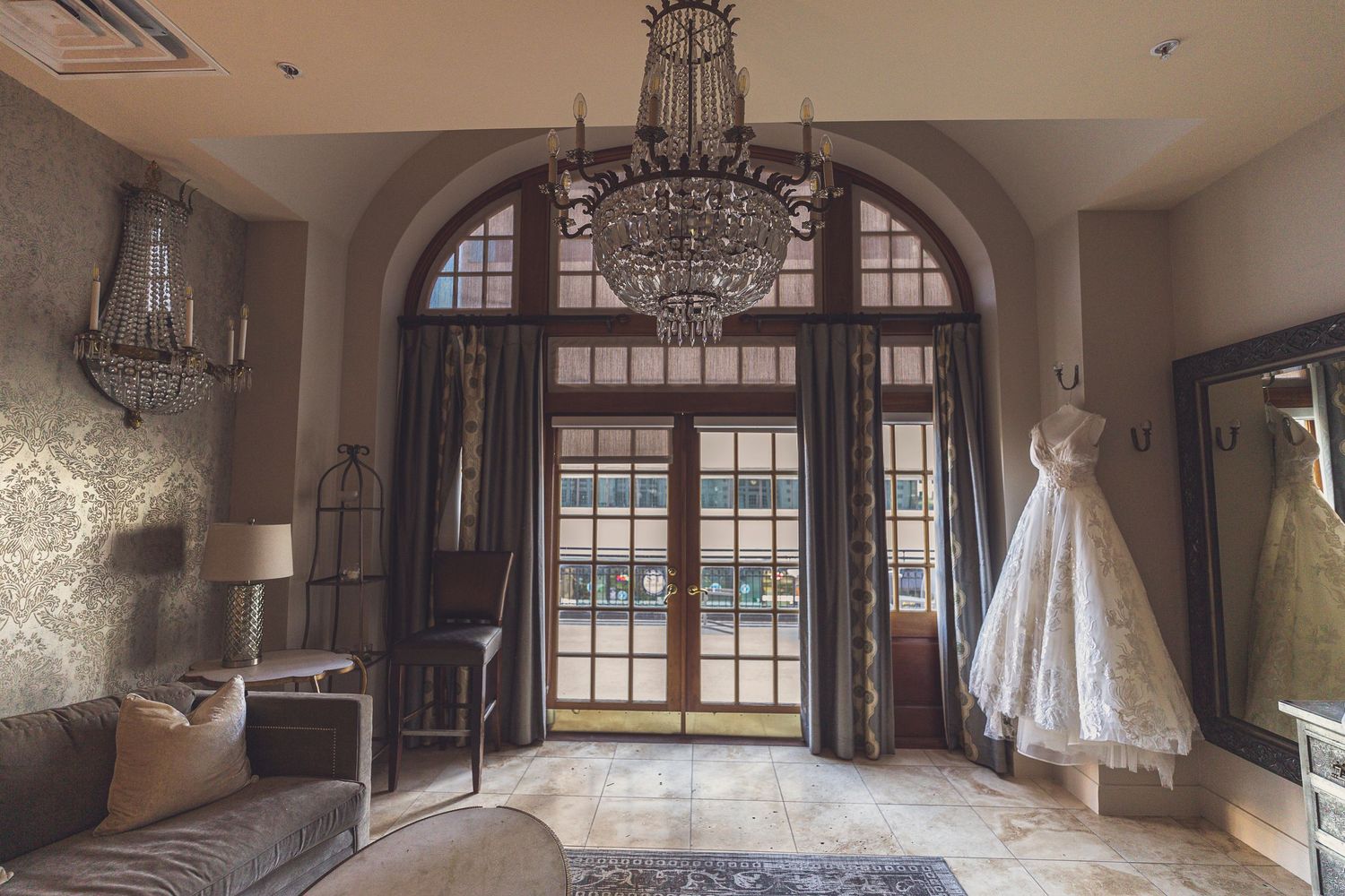 Elegant foyer with crystal chandelier and wedding dress hanging by arched French doors.