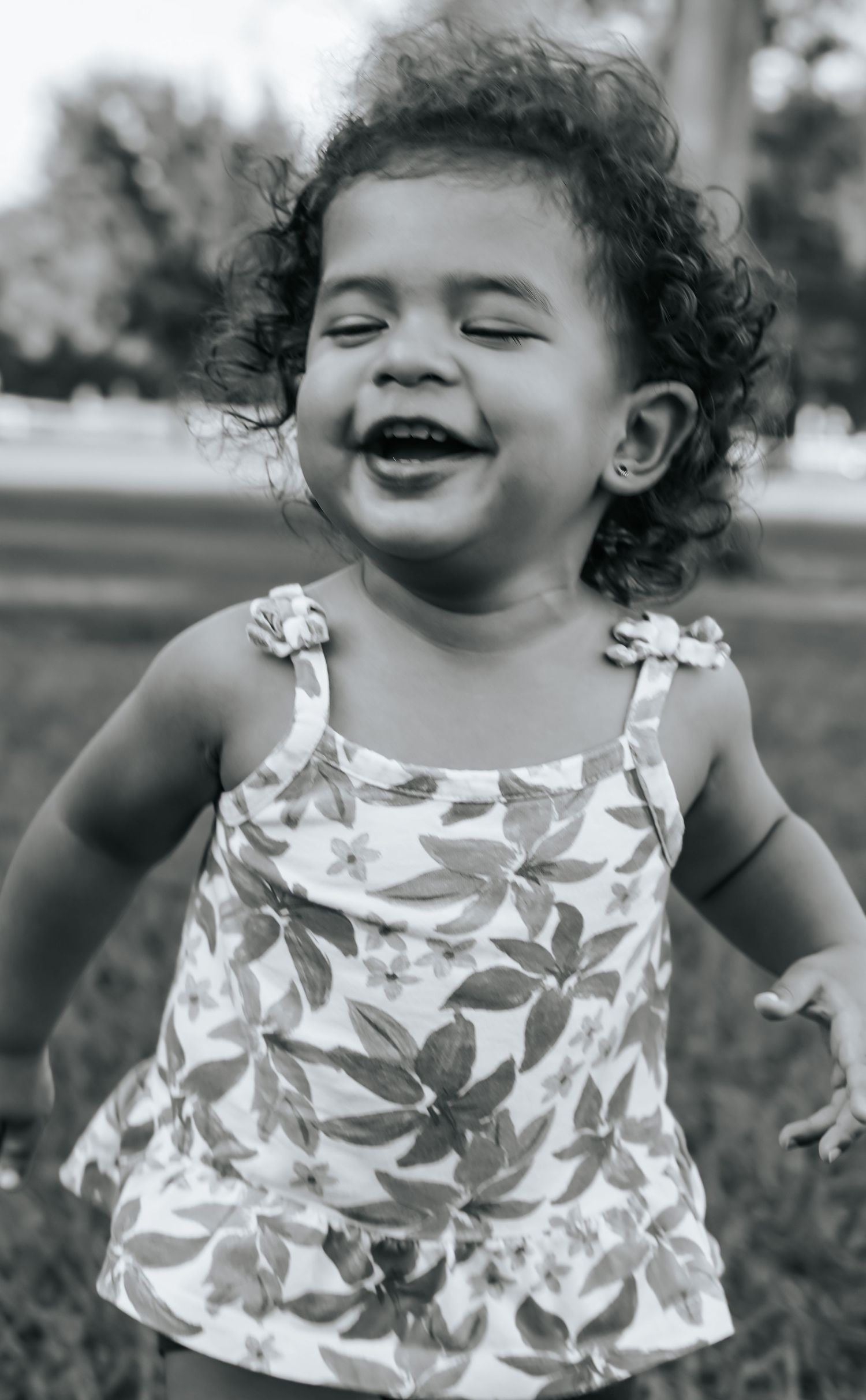 A joyful toddler laughs while wearing a floral tank top in this black and white portrait.
