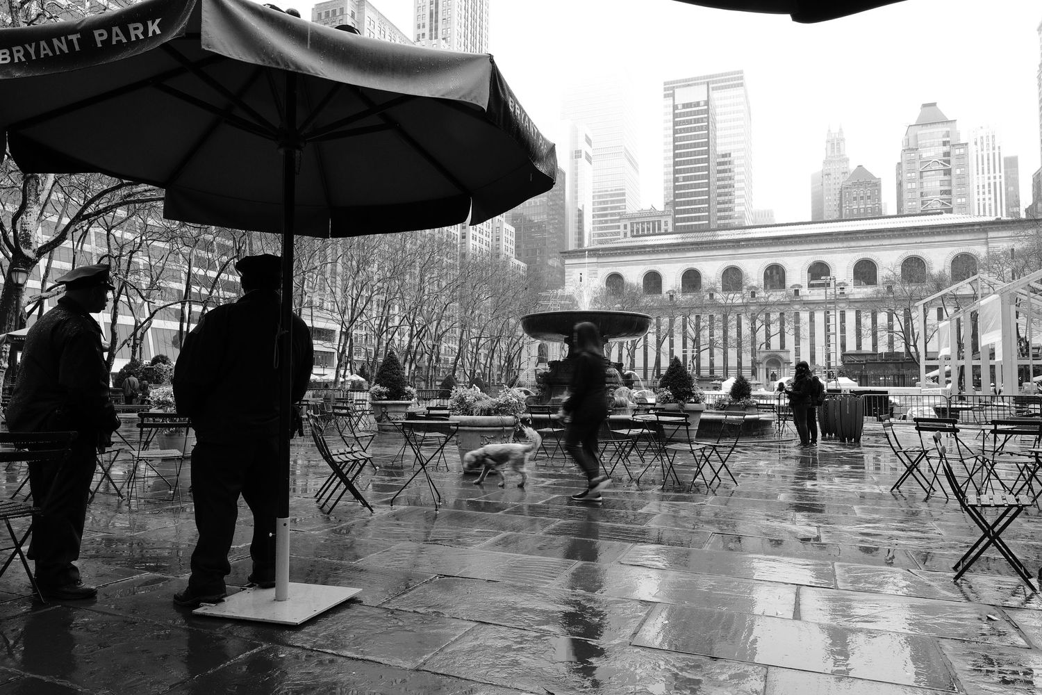 Rainy day scene at Bryant Park with umbrellas and Manhattan buildings in the background.