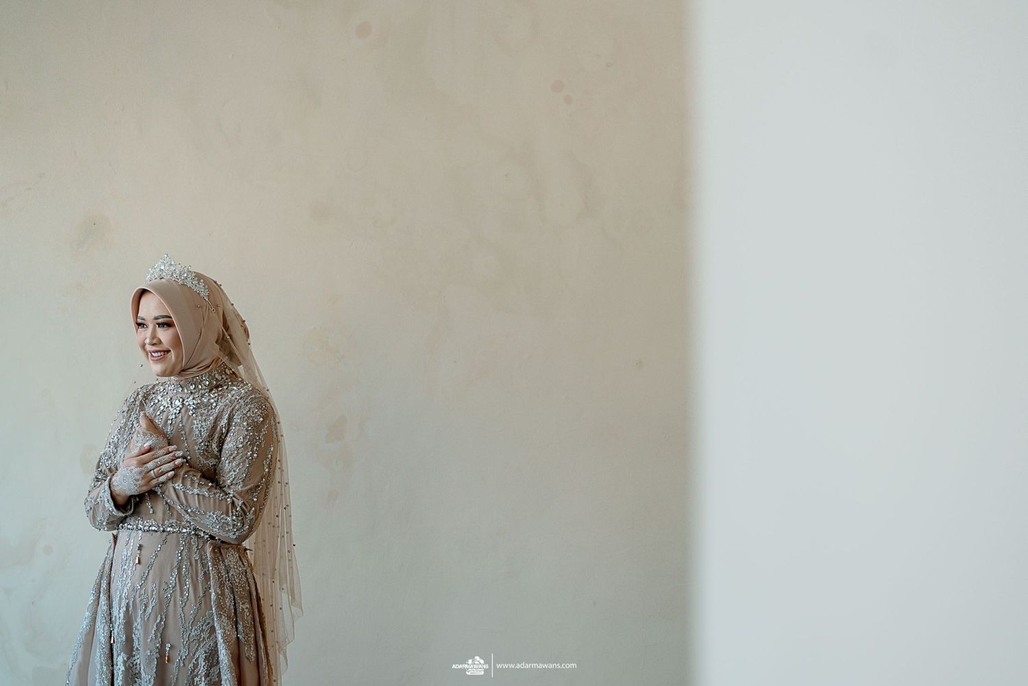 A person in elegant attire poses against a light neutral wall.