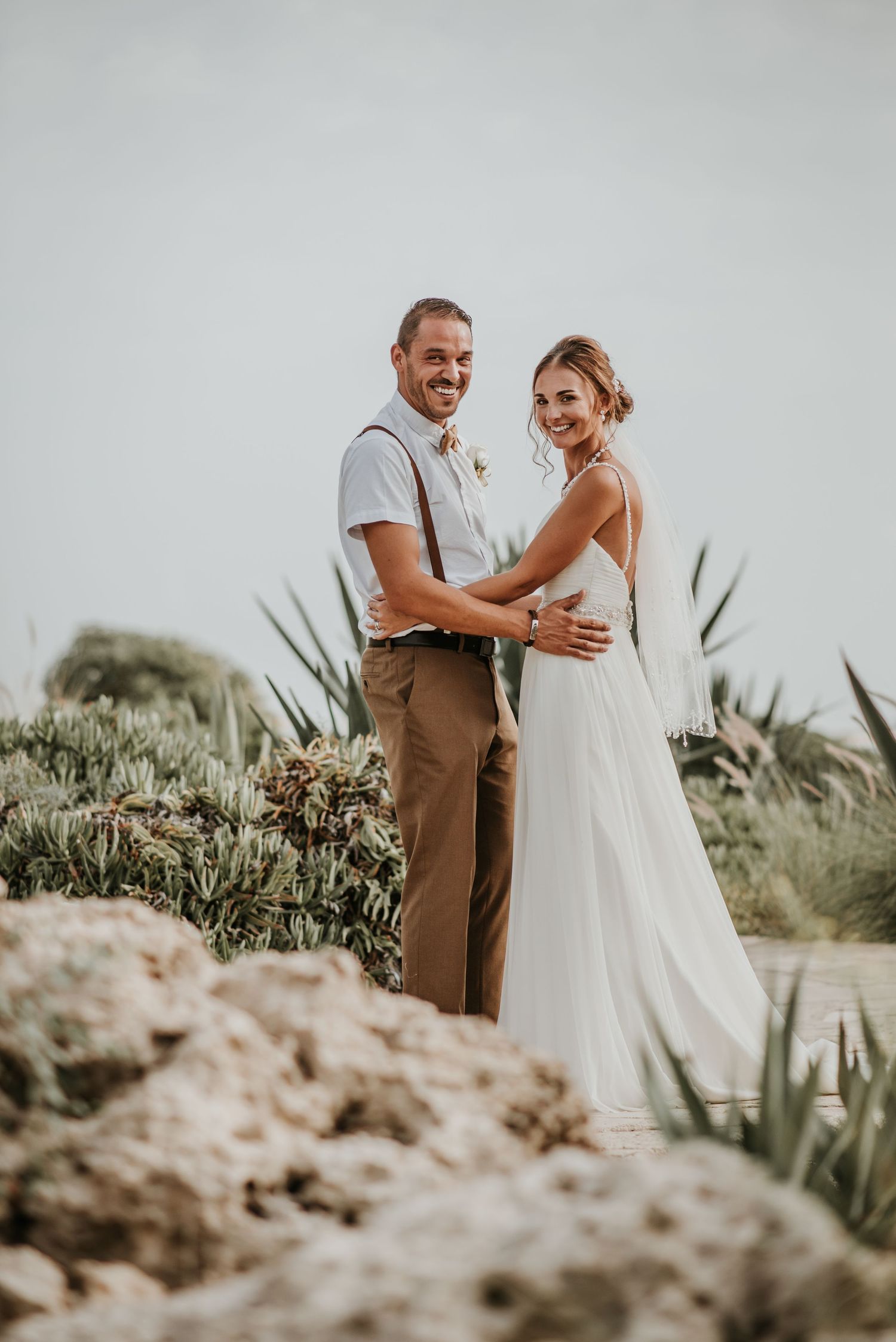 Desert botanical garden wedding portrait with couple surrounded by succulents and natural rock formations.