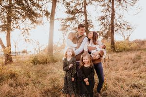 Family of five posing in a sunlit forest clearing during golden hour in autumn.