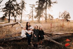 Mother sitting on a fallen log with four children in a golden autumn field at sunset.