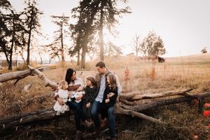 Family of five sitting together on a fallen log in a sunlit autumn field at golden hour.