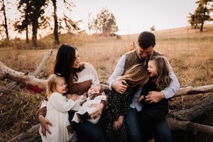 Loving family laughing and embracing on a log in a golden autumn field at sunset.