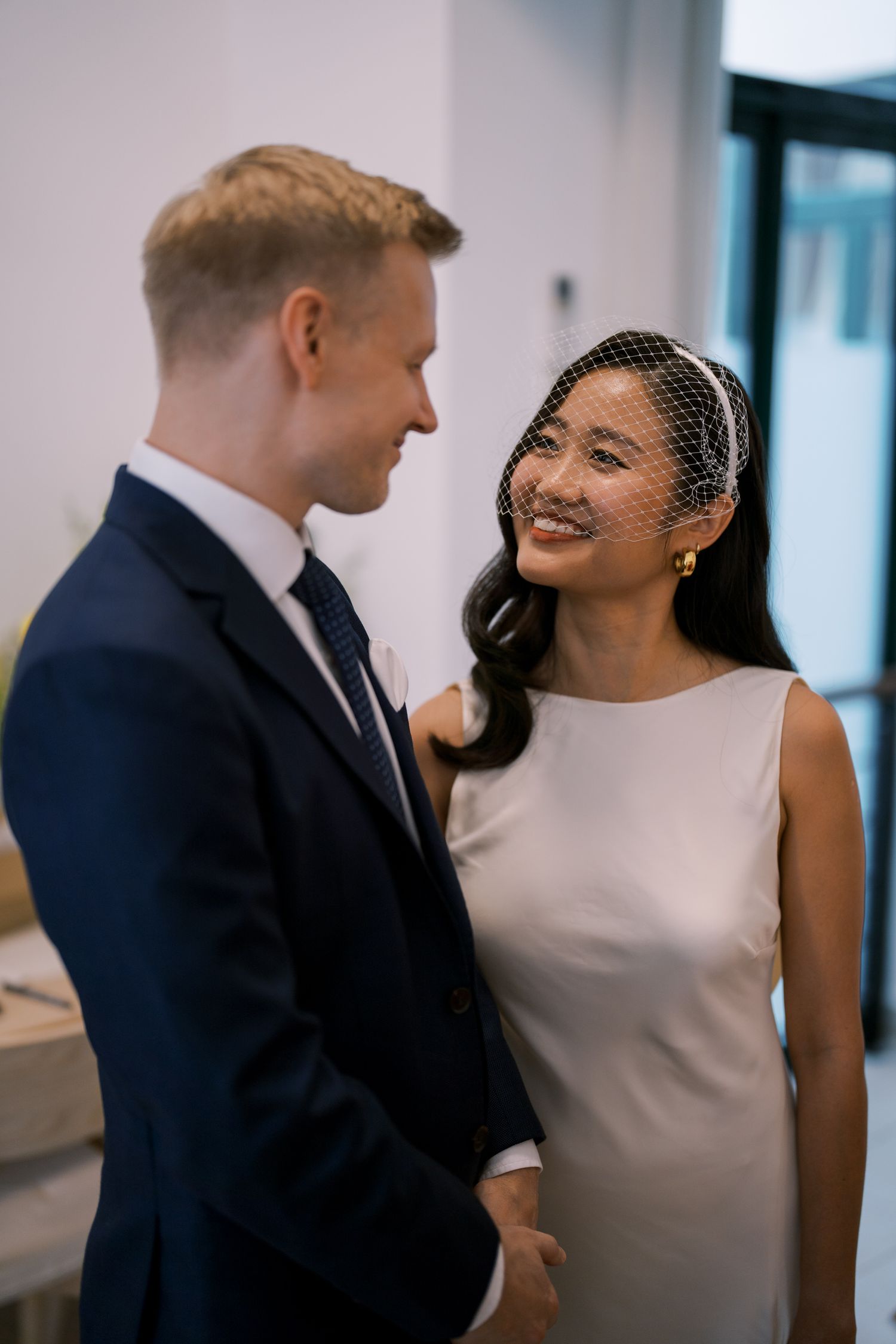 A couple shares a joyful moment in a bright indoor space, with the bride wearing a classic white dress.