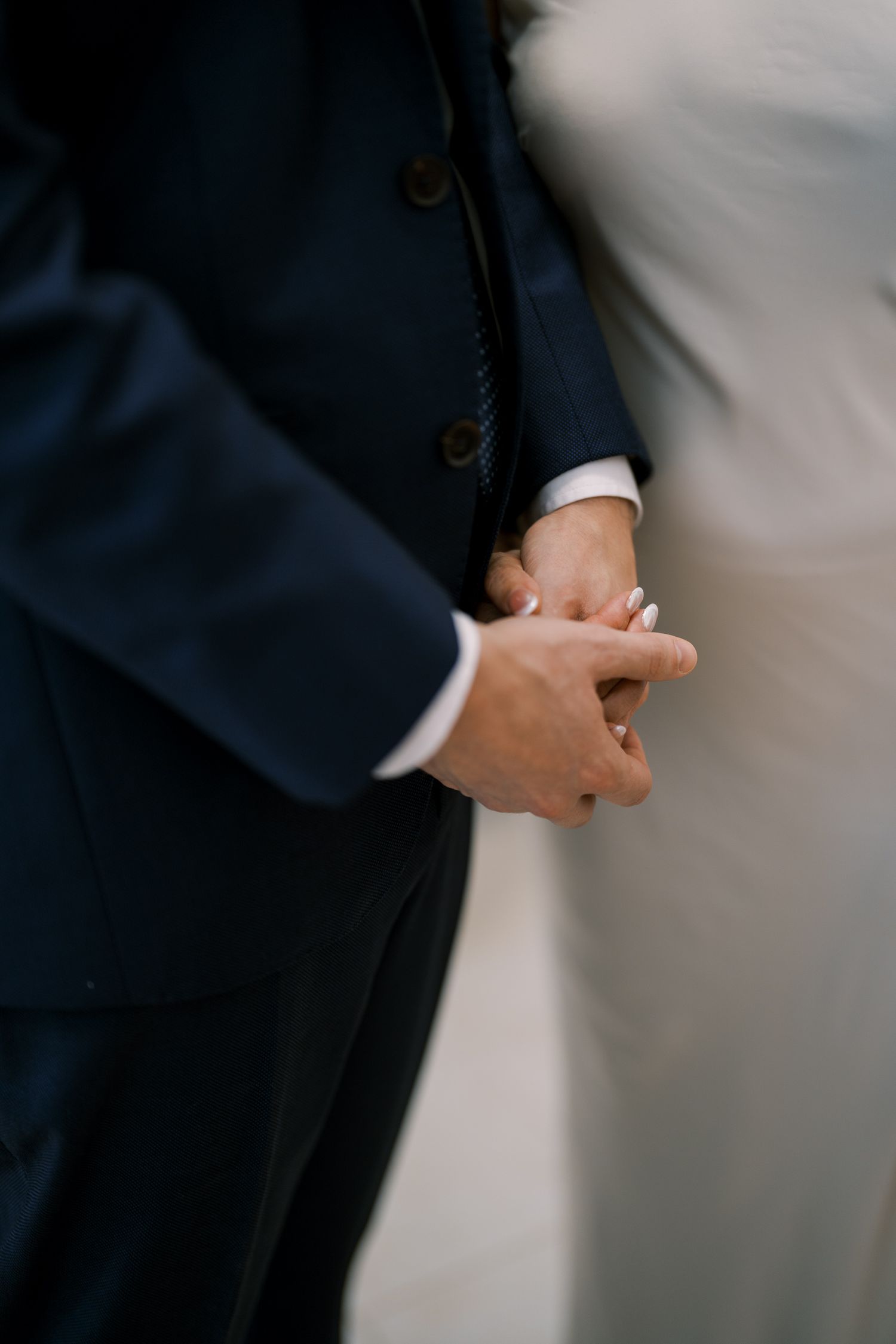 Close-up of hands adjusting a navy blue suit jacket sleeve in an elegant setting.