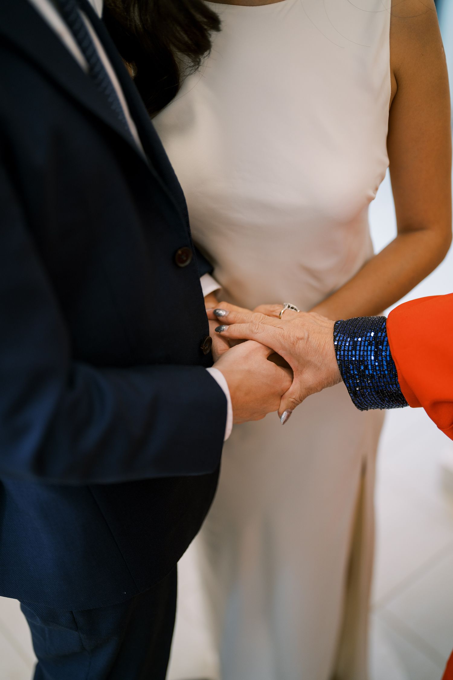 Close-up of hands during a ring exchange ceremony with the bride in a sleeveless white dress.