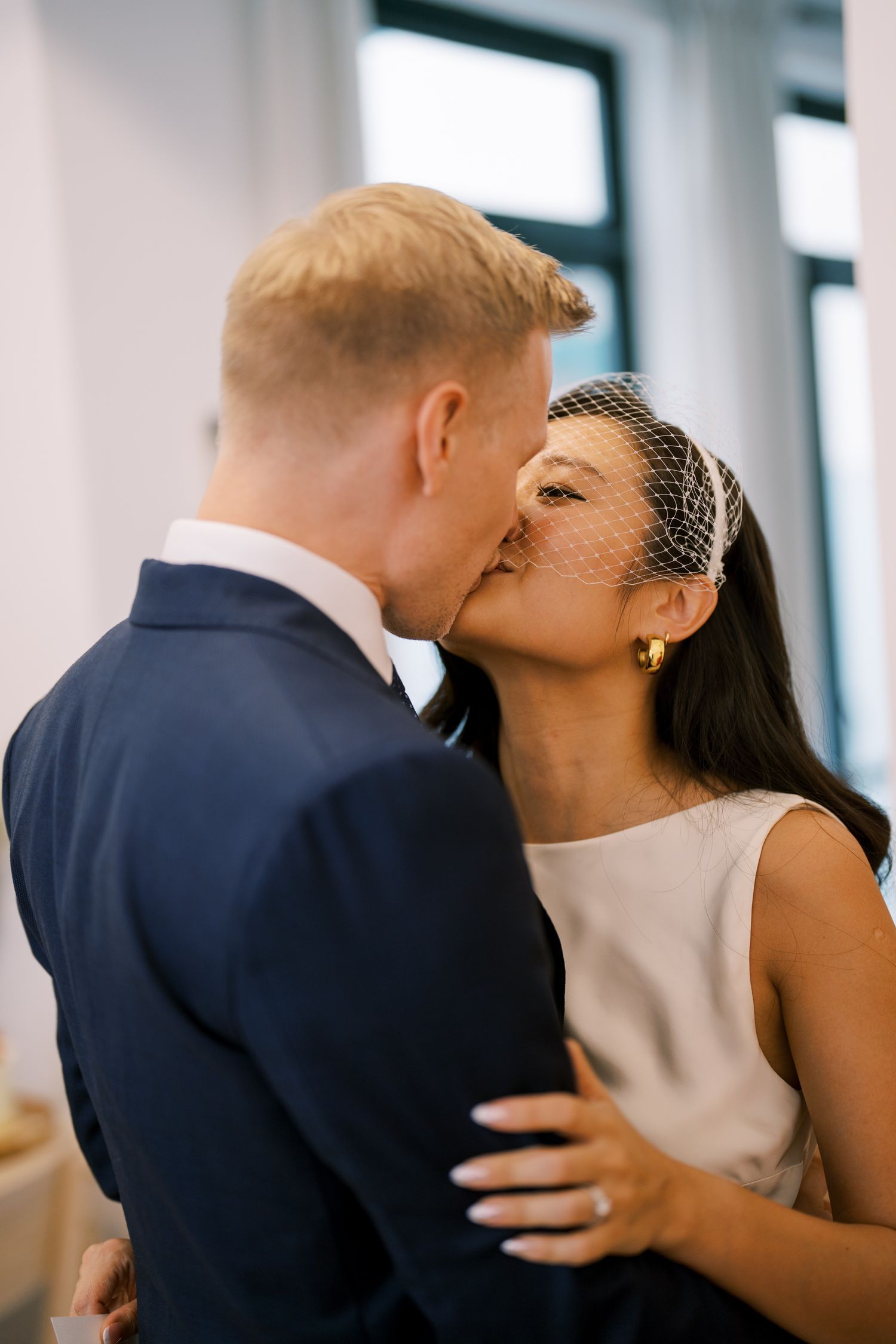 A romantic kiss shared between newlyweds in a bright, modern ceremony space.