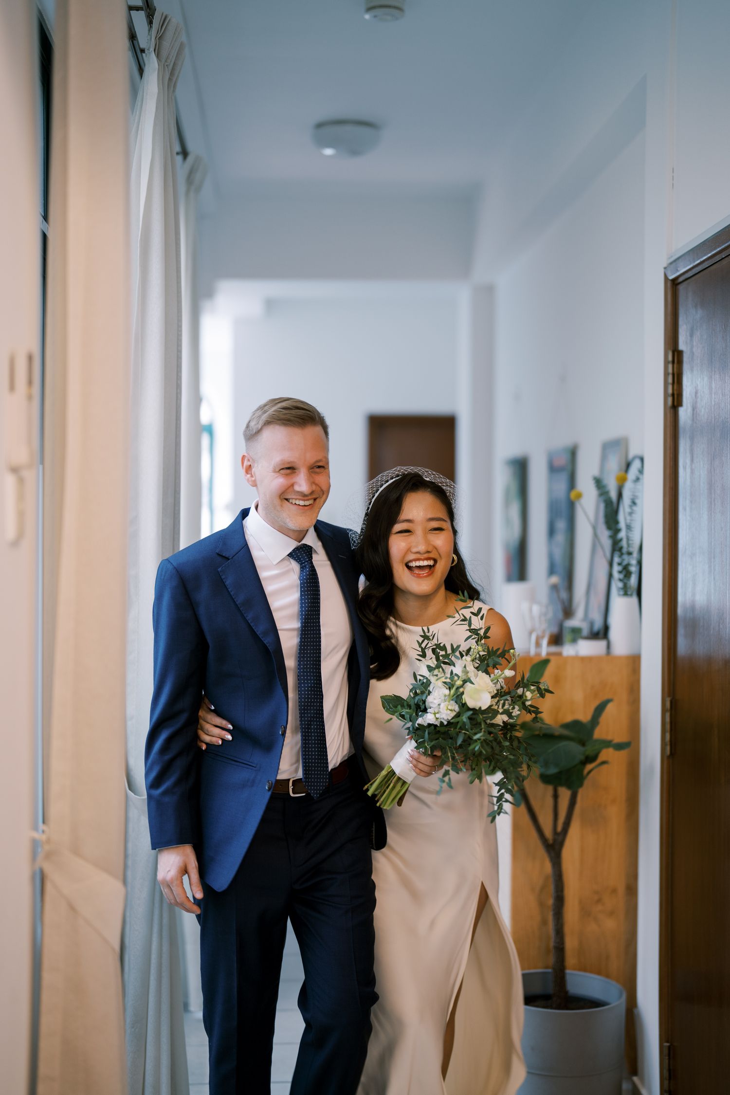 Couple sharing laughter while walking down a minimalist white corridor.