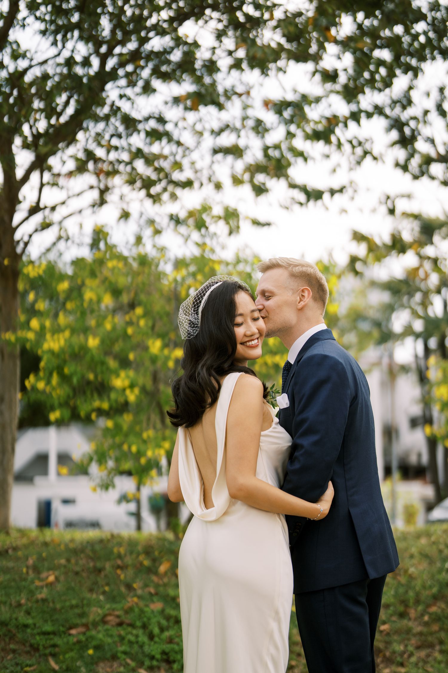 A romantic moment captured between a couple in a park setting with lush green trees in the background.