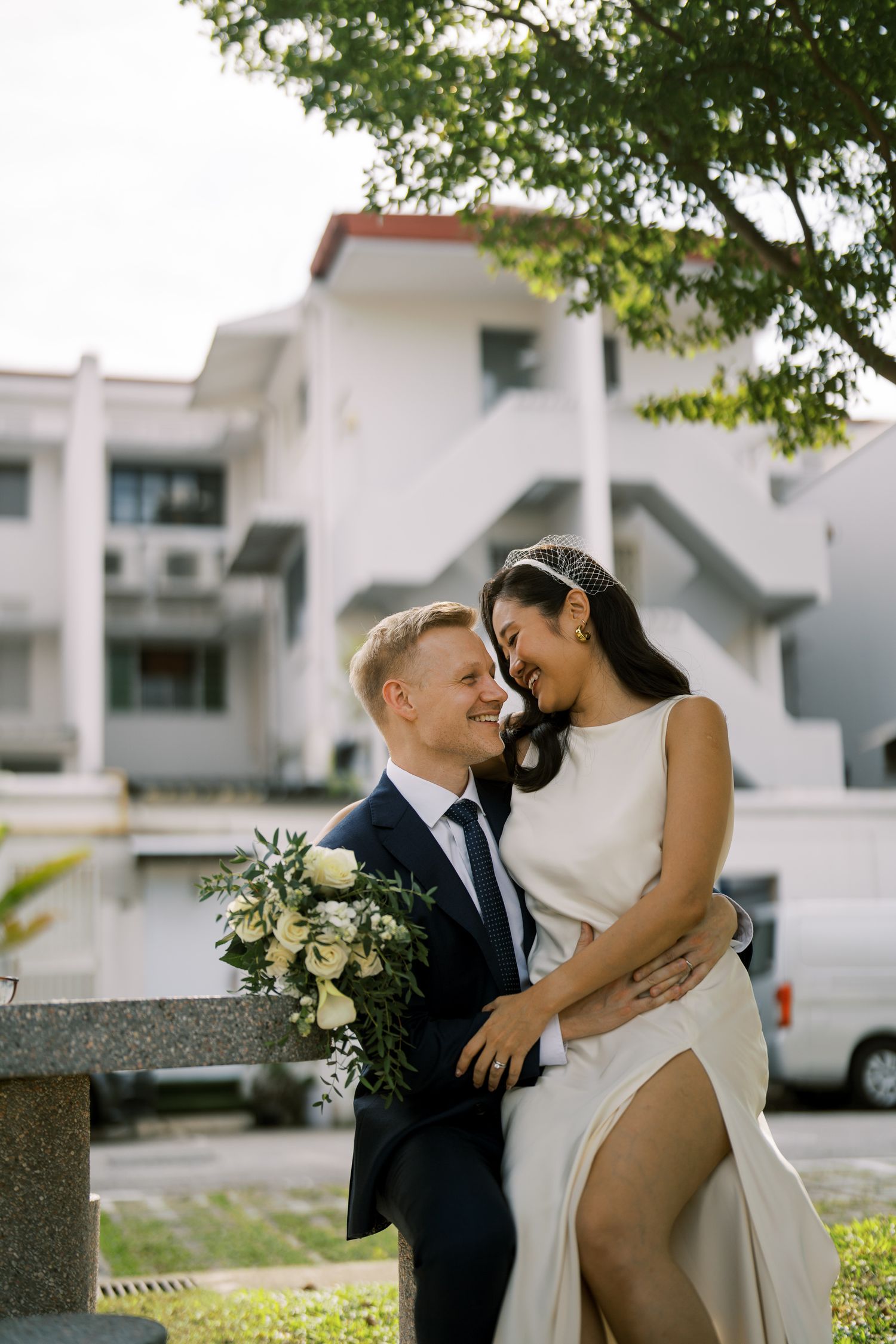 A couple in wedding attire shares intimate moments in an urban garden setting.