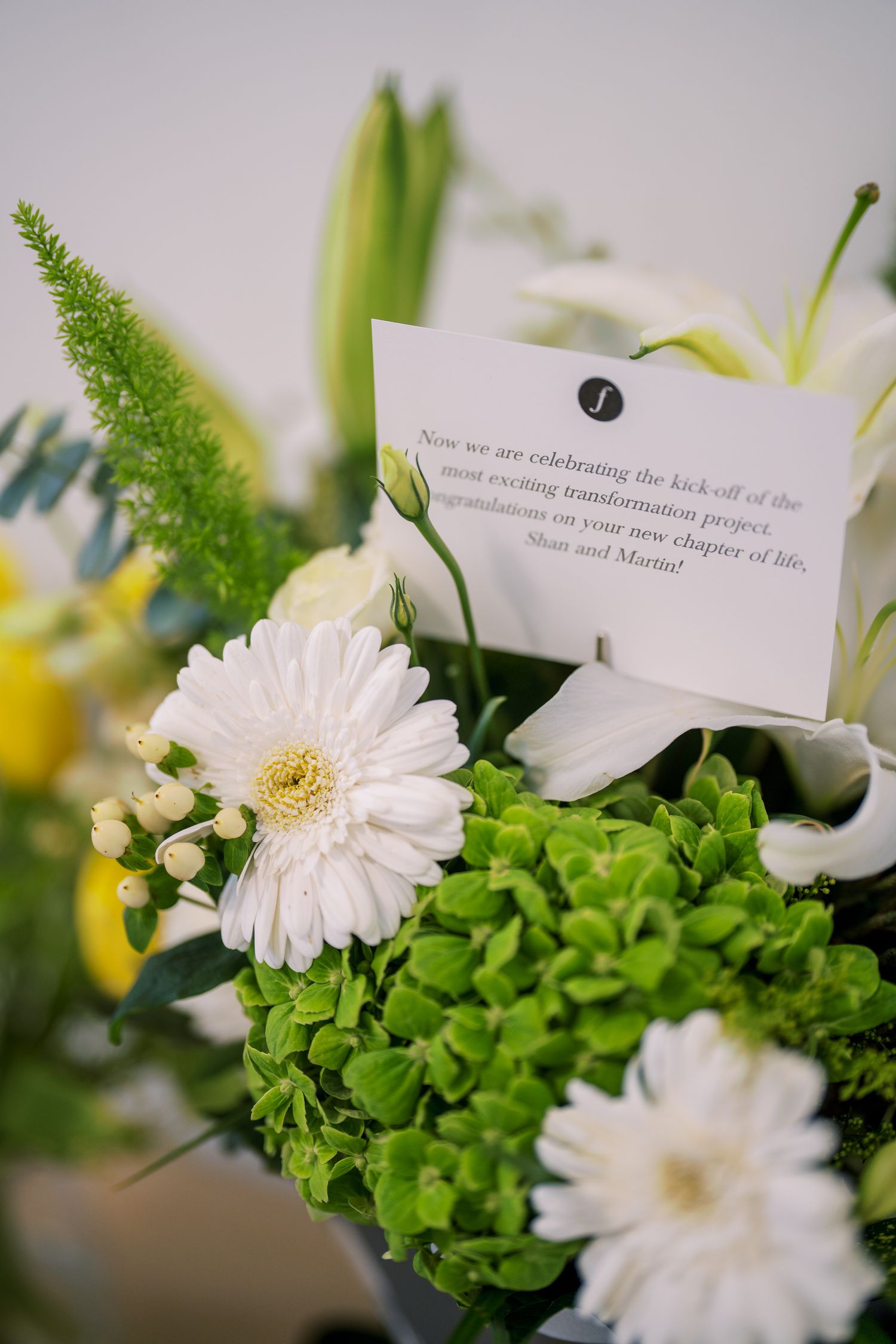 Elegant floral arrangement with white gerbera daisies and green hydrangeas featuring a message card.