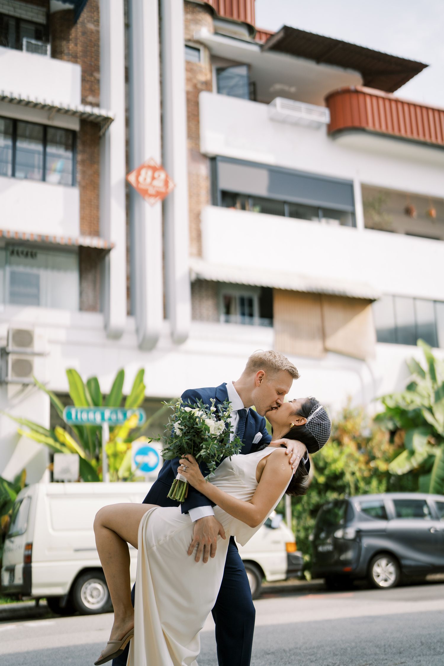 A series of romantic dip poses between newlyweds outside a modern building with palm plants.