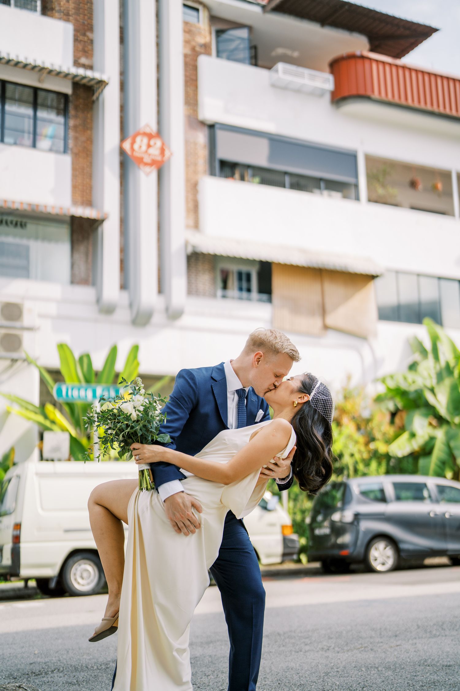 Wedding couple performing a dramatic dip pose against an architectural backdrop with tropical plants.