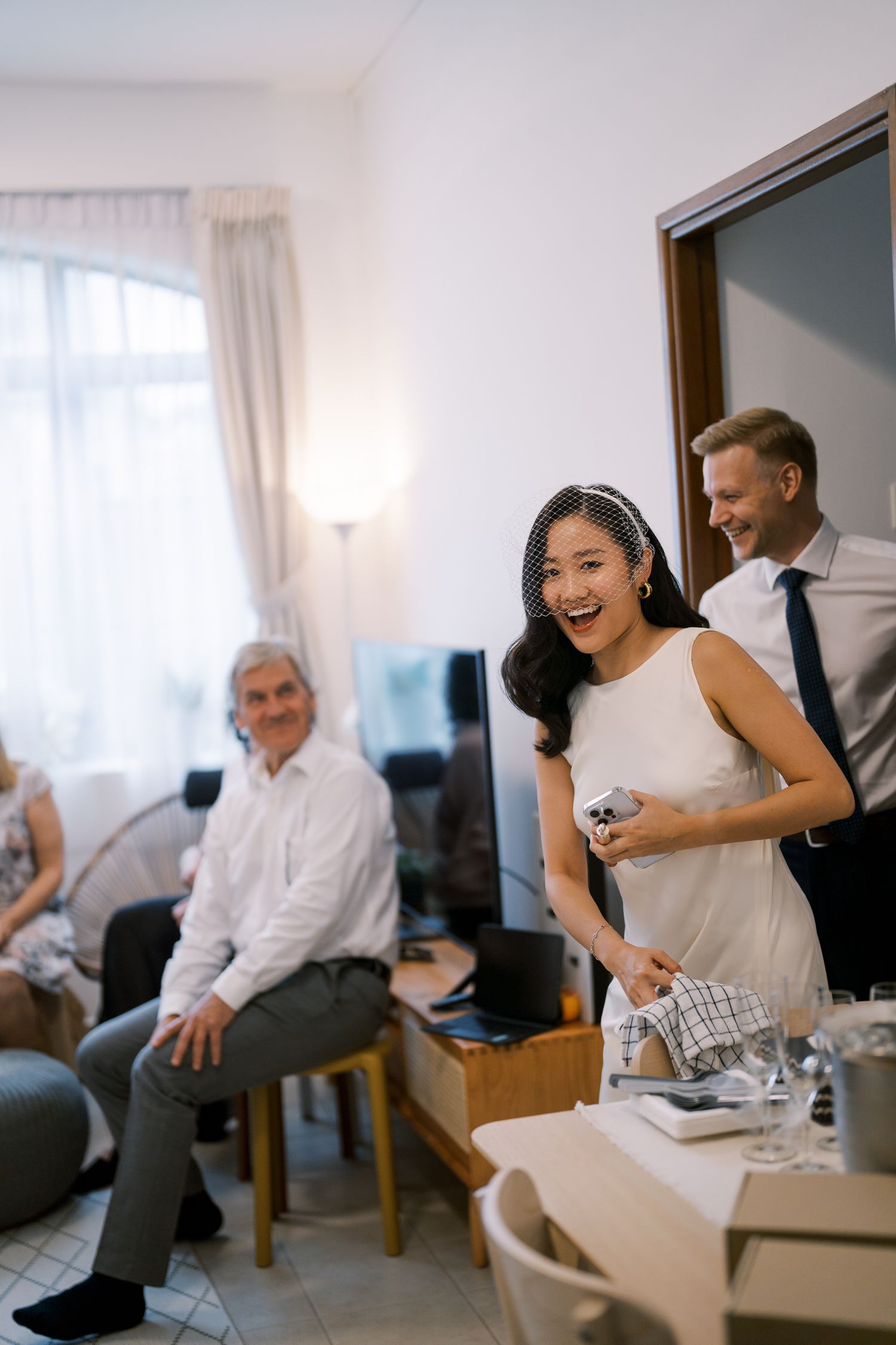 Wedding party members laughing and embracing in a bright indoor setting.