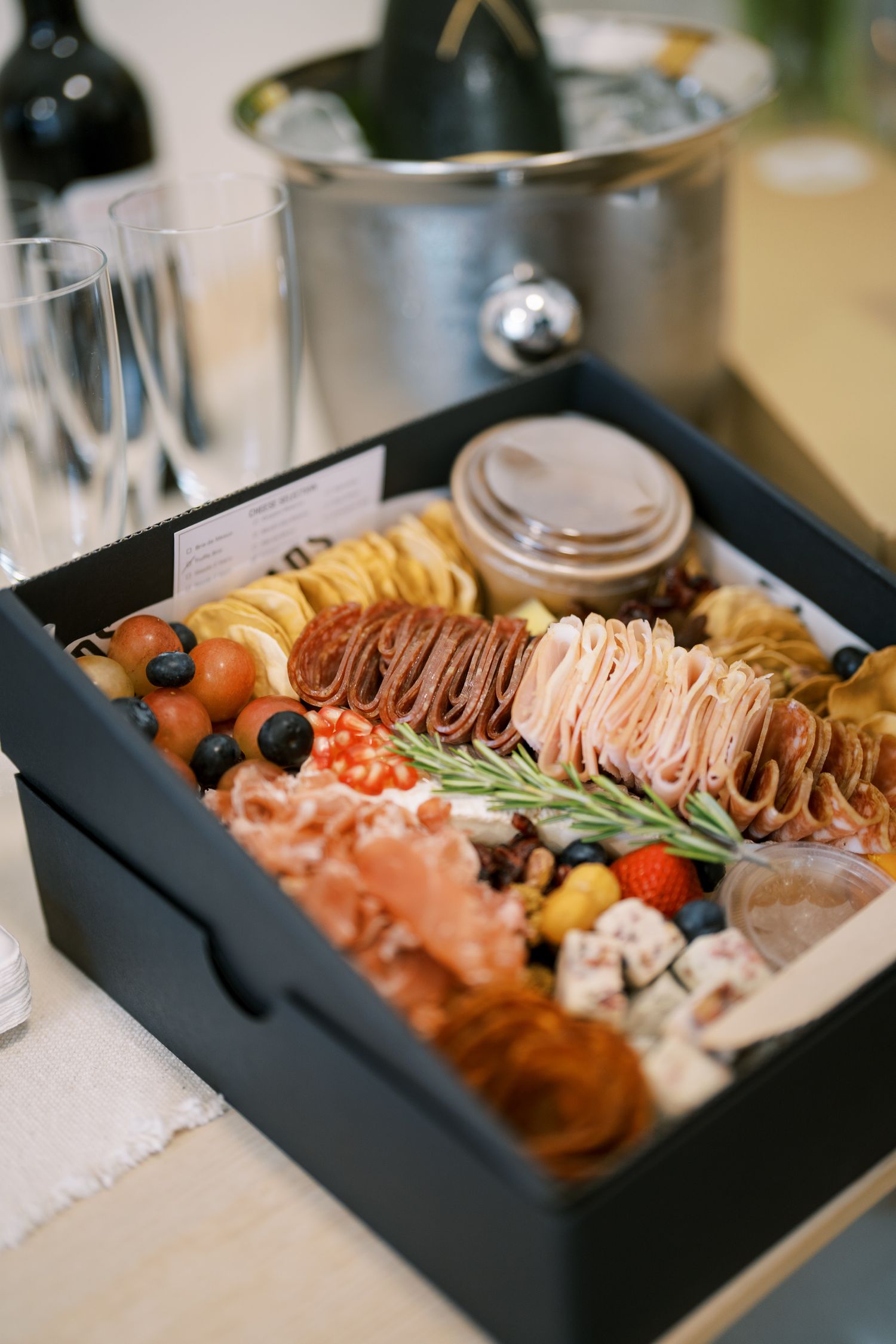 Gourmet charcuterie board with meats, cheeses and garnishes arranged in a black serving tray.
