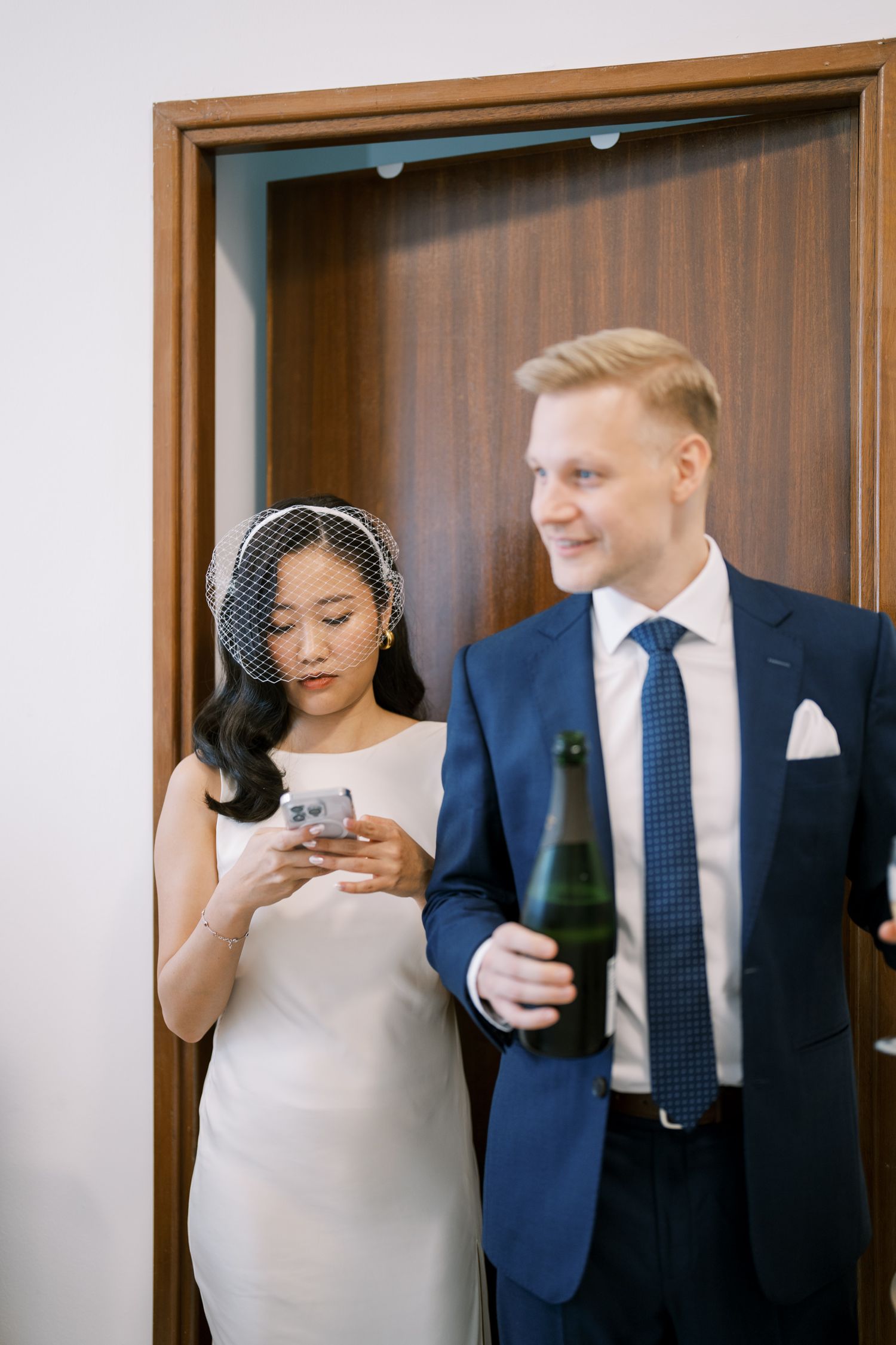 A couple shares a moment before their wedding ceremony, with the bride checking her phone.