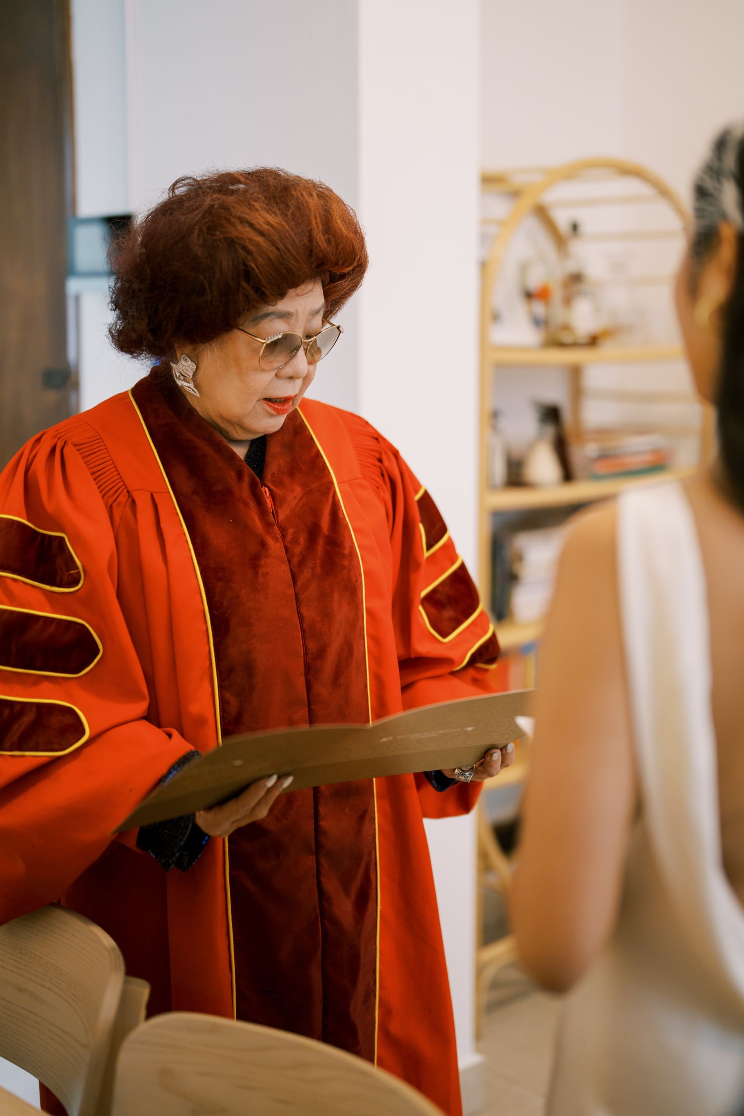 An officiant in a red academic robe reviews ceremony documents.