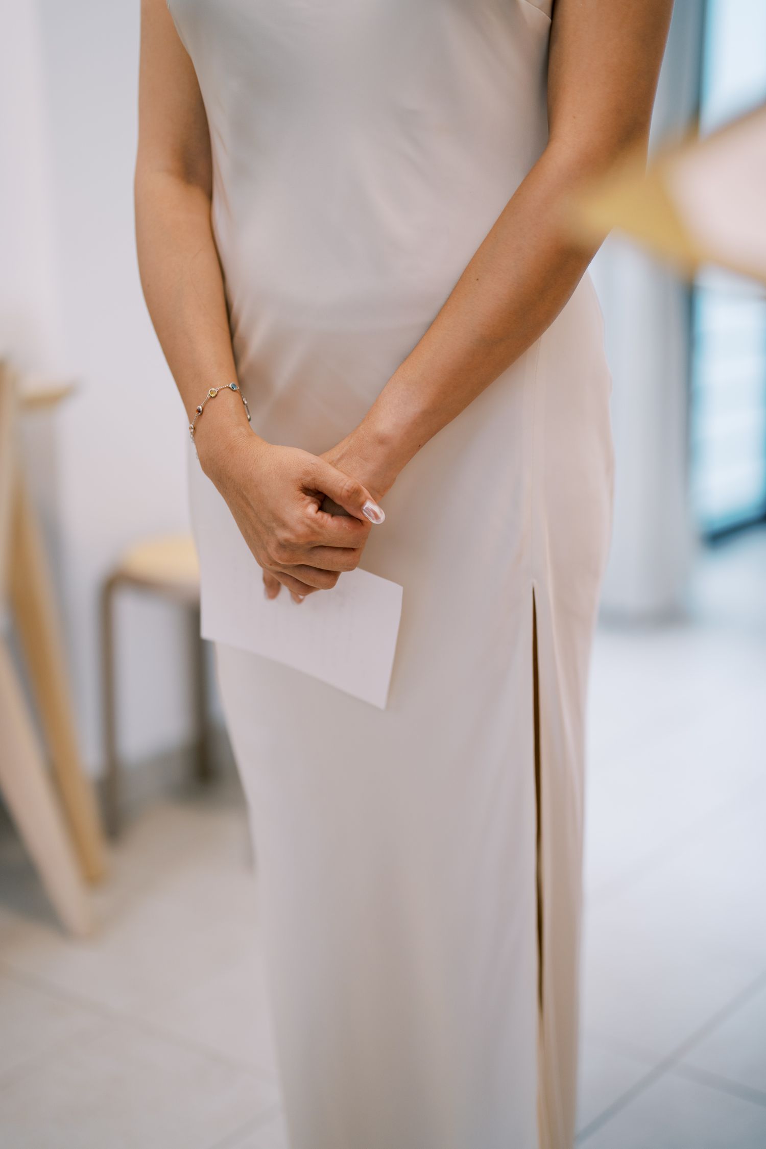 Close-up of hands holding a white card against an elegant white wedding dress.