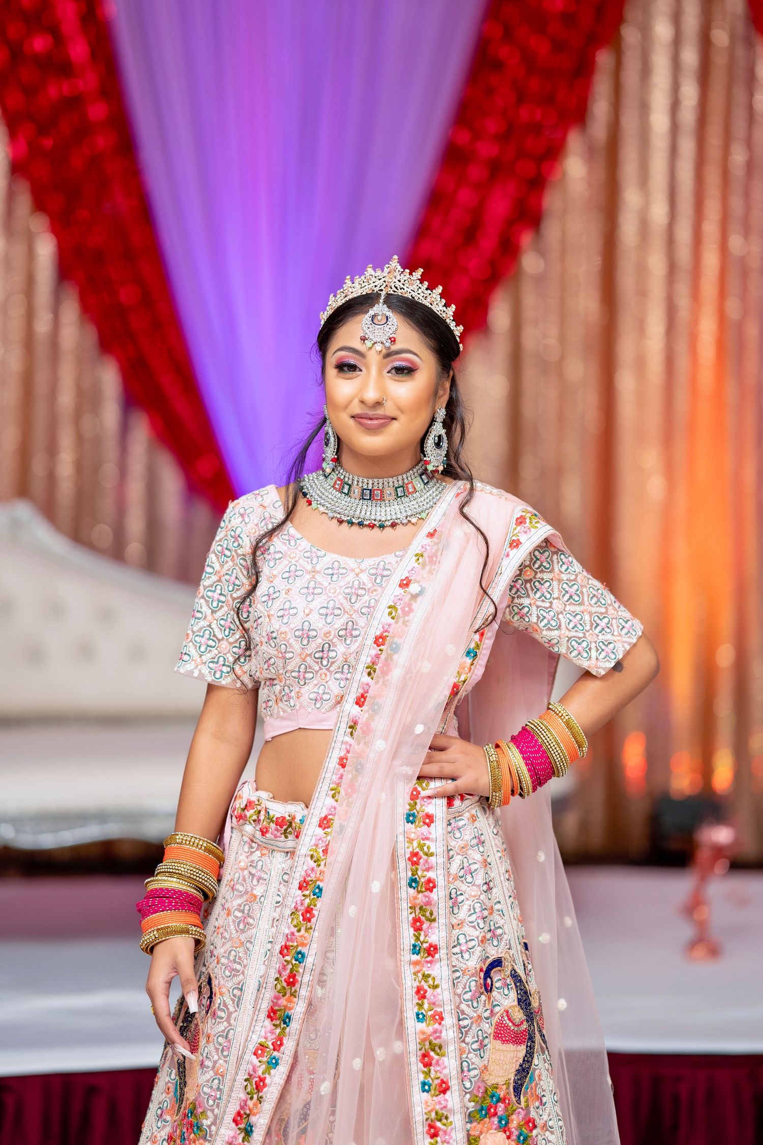 Festive occasion outfit featuring pink embroidered lehenga with silver jewelry against draped backdrop.