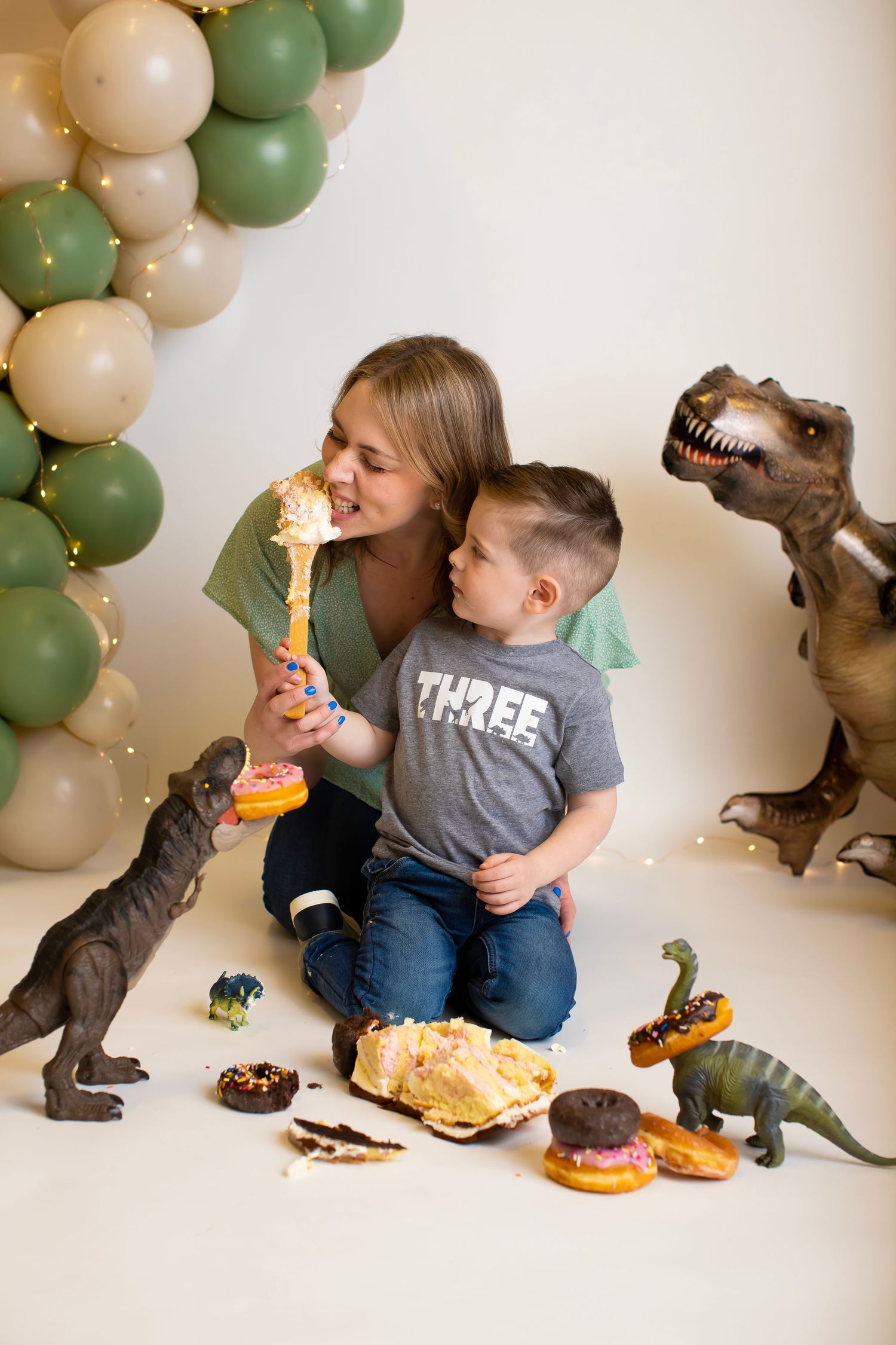 Joyful dinosaur themed photoshoot with treats and green balloon decorations.