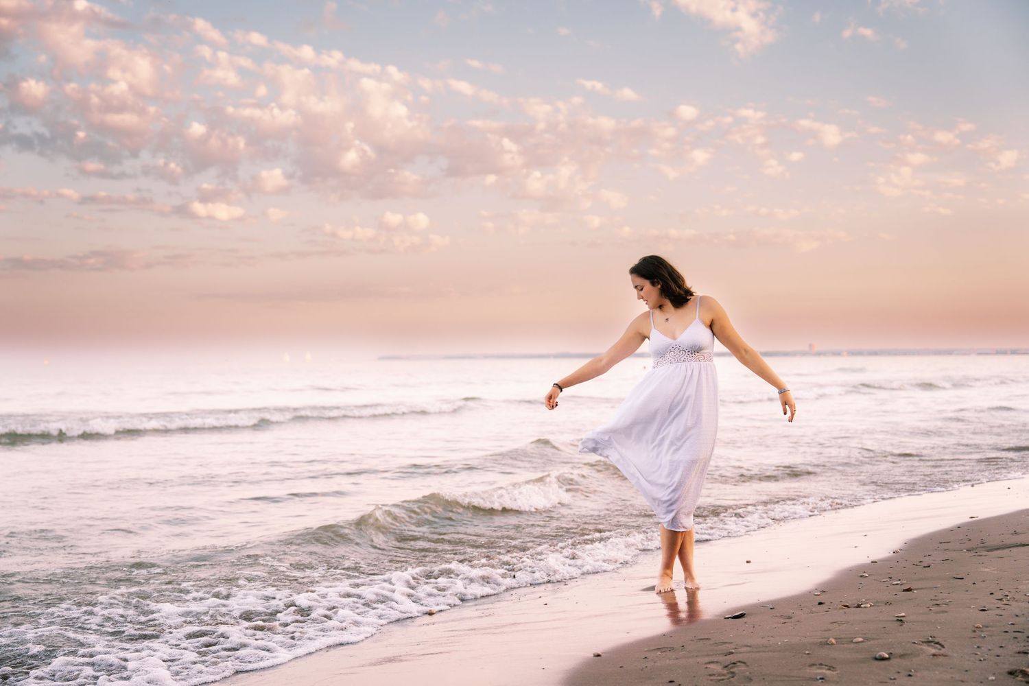 Portrait of woman in white dress on windy beach with pink-lit sky, shot by Milwaukee senior and family photographer Rachel Dickman.