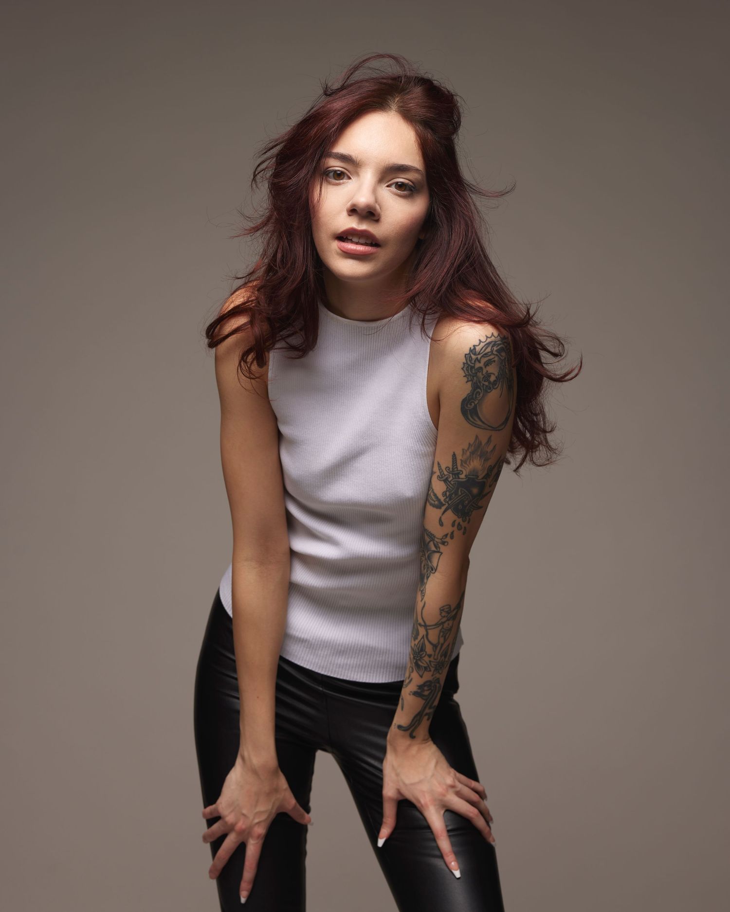 Edgy portrait of a person in sleeveless top with visible arm tattoos against dark background.