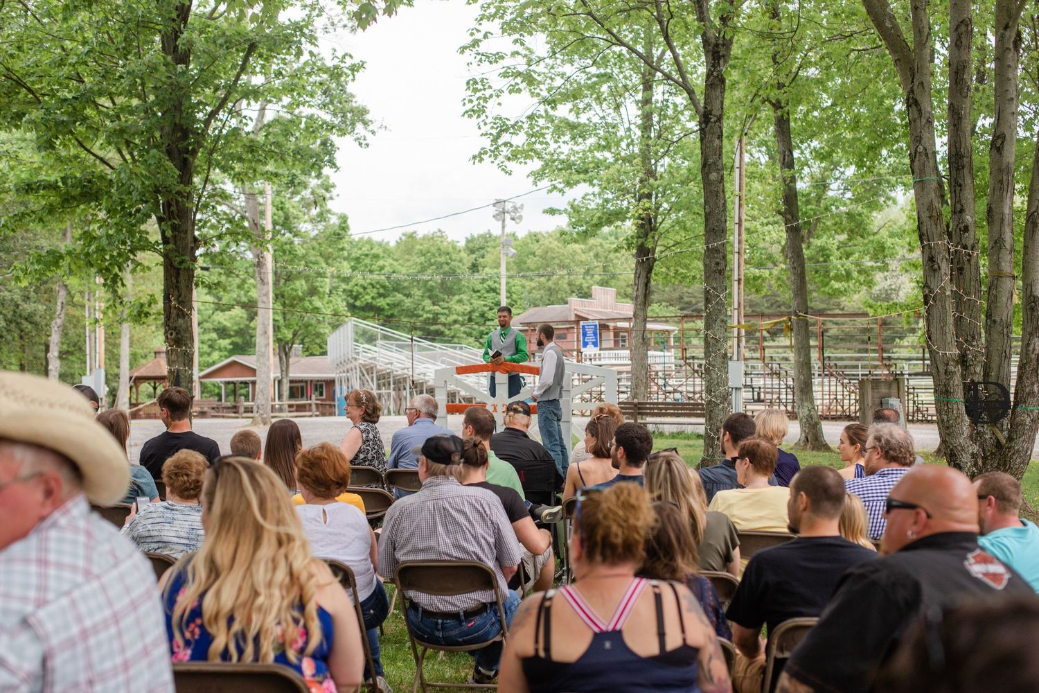 Wedding guests gathered under trees for an outdoor ceremony.