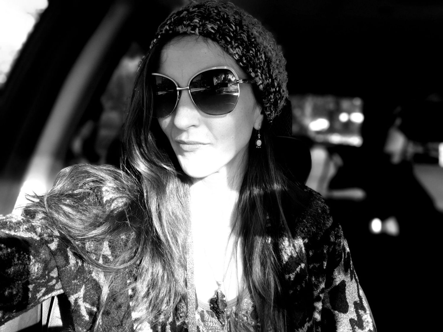 Black and white portrait with sunglasses and patterned headscarf in dramatic lighting.