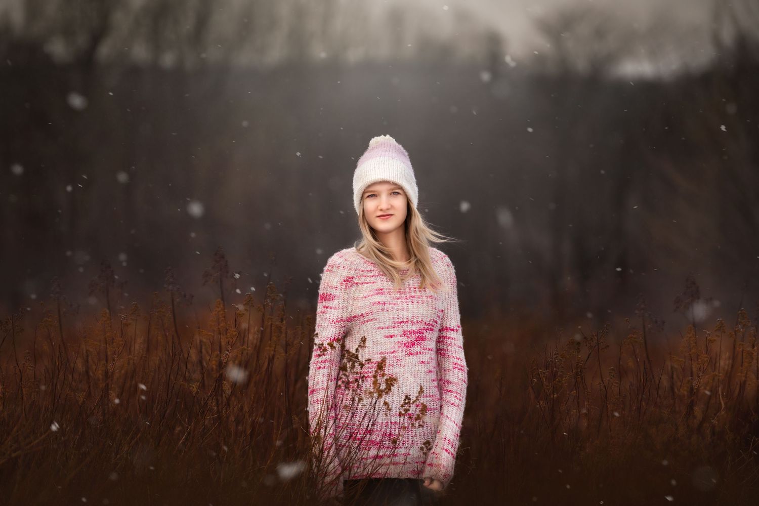Winter portrait in field with snow falling and warm pink sweater.