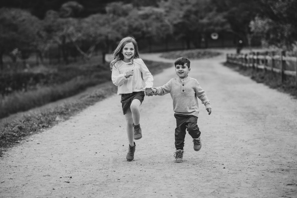 Black and white photo of children running and playing together on a path outdoors.