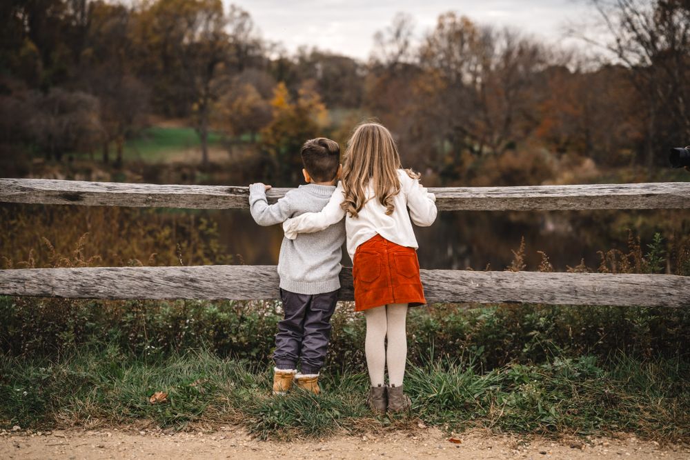 Children sitting together on a stone wall during autumn with trees in background.