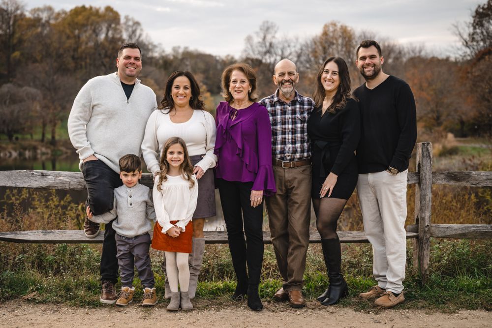 Family group poses together outdoors with fall foliage and natural scenery.