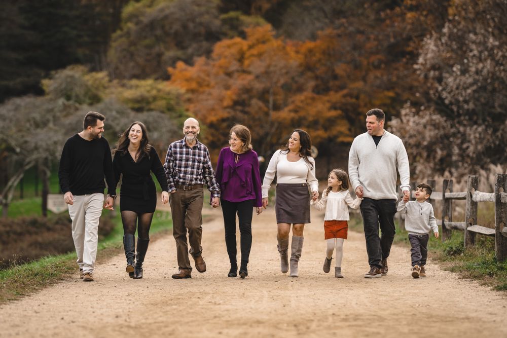 Group walking together holding hands along autumn path with trees in background.