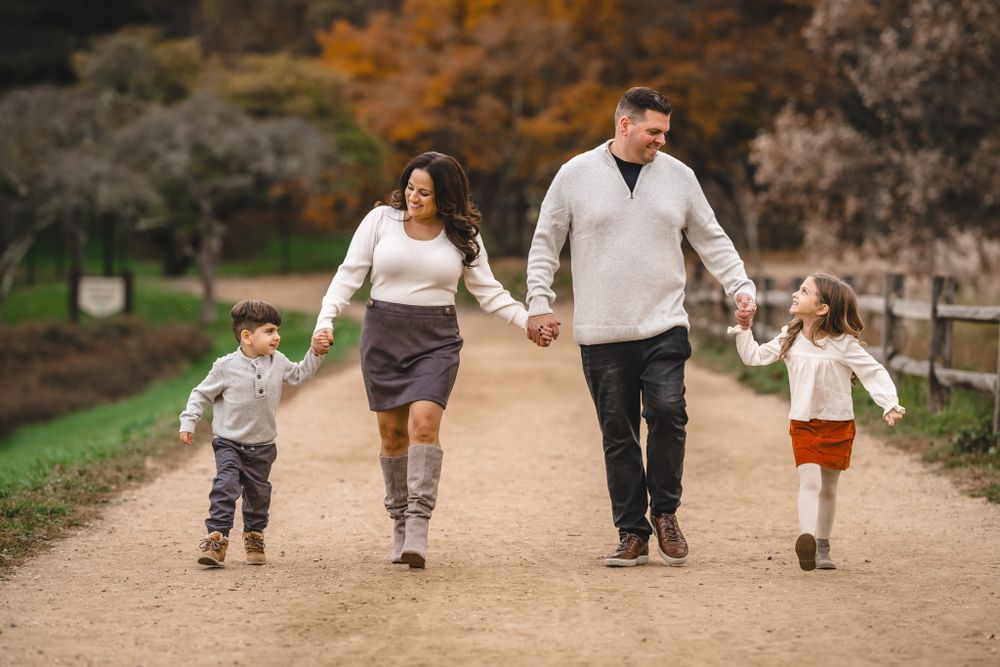 Family members walk and play together on dirt path during fall photo session.