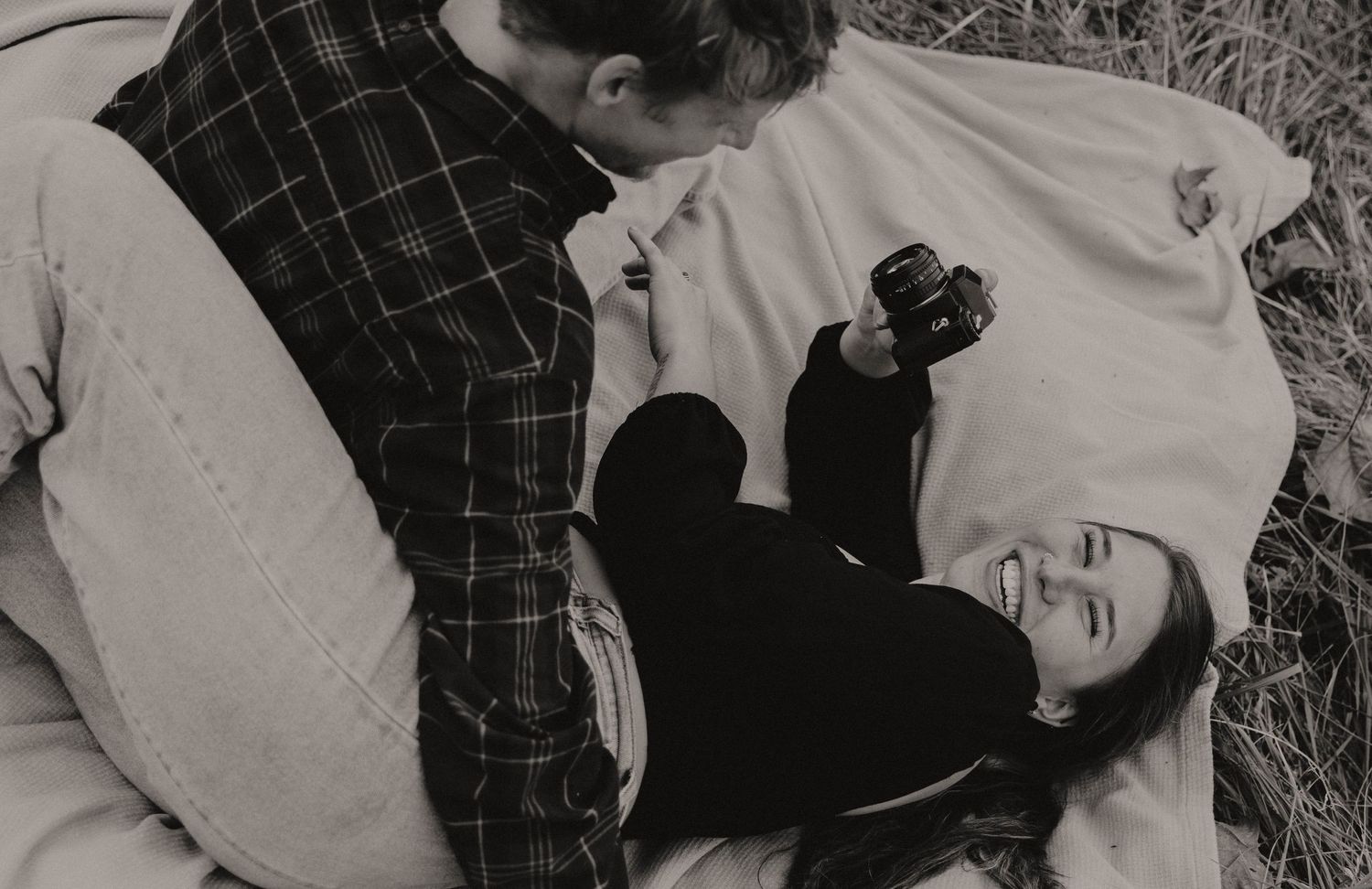 A black and white photo of a couple lying on a blanket outdoors sharing an intimate moment.