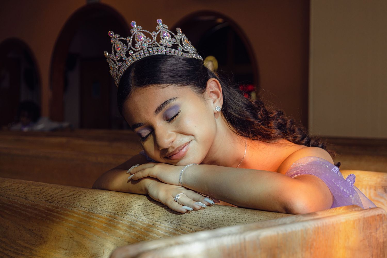 A soft portrait featuring a purple gown and tiara in warm ambient lighting.