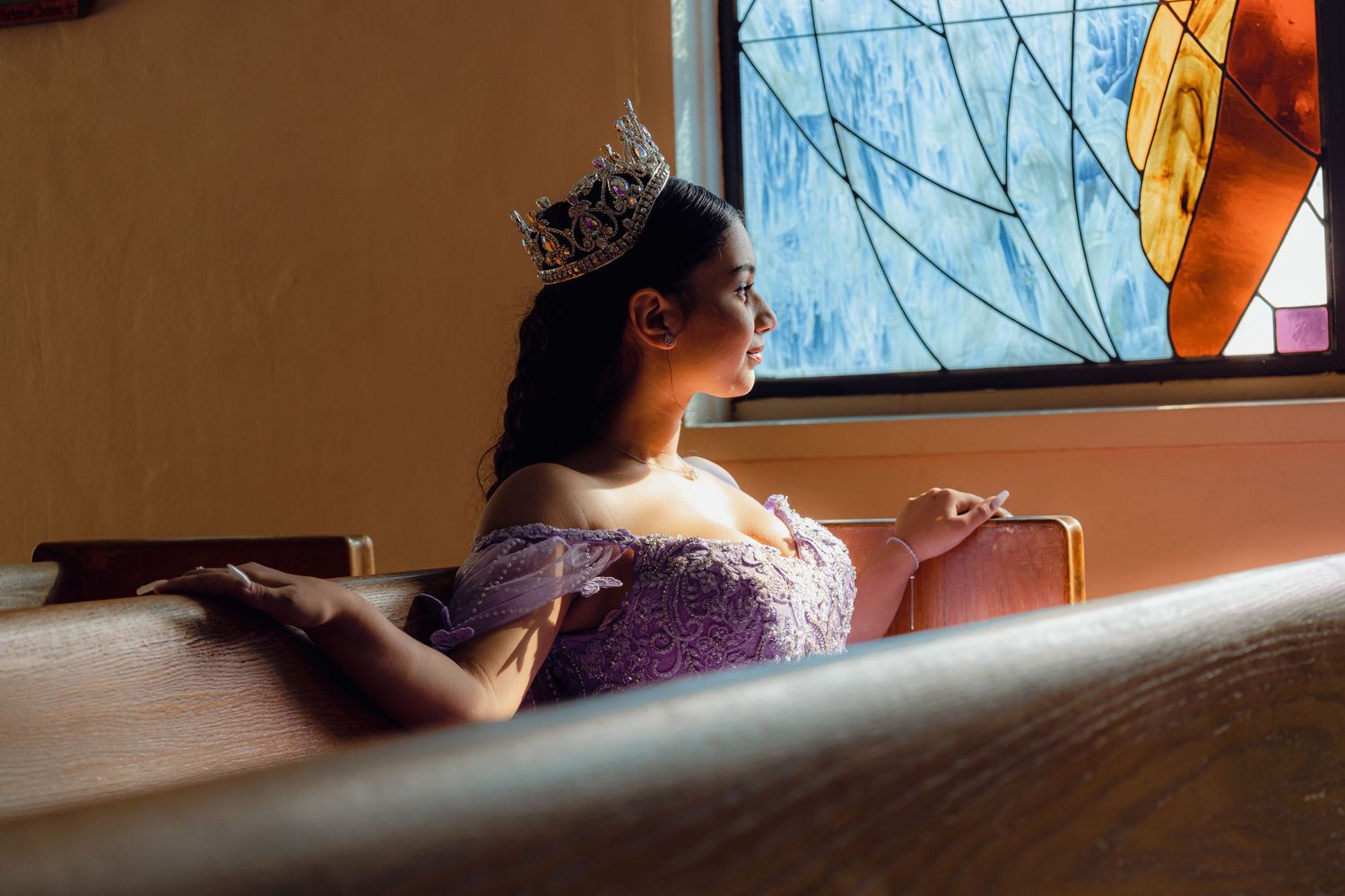 An artistic side profile portrait near a window featuring a purple formal dress and crown.