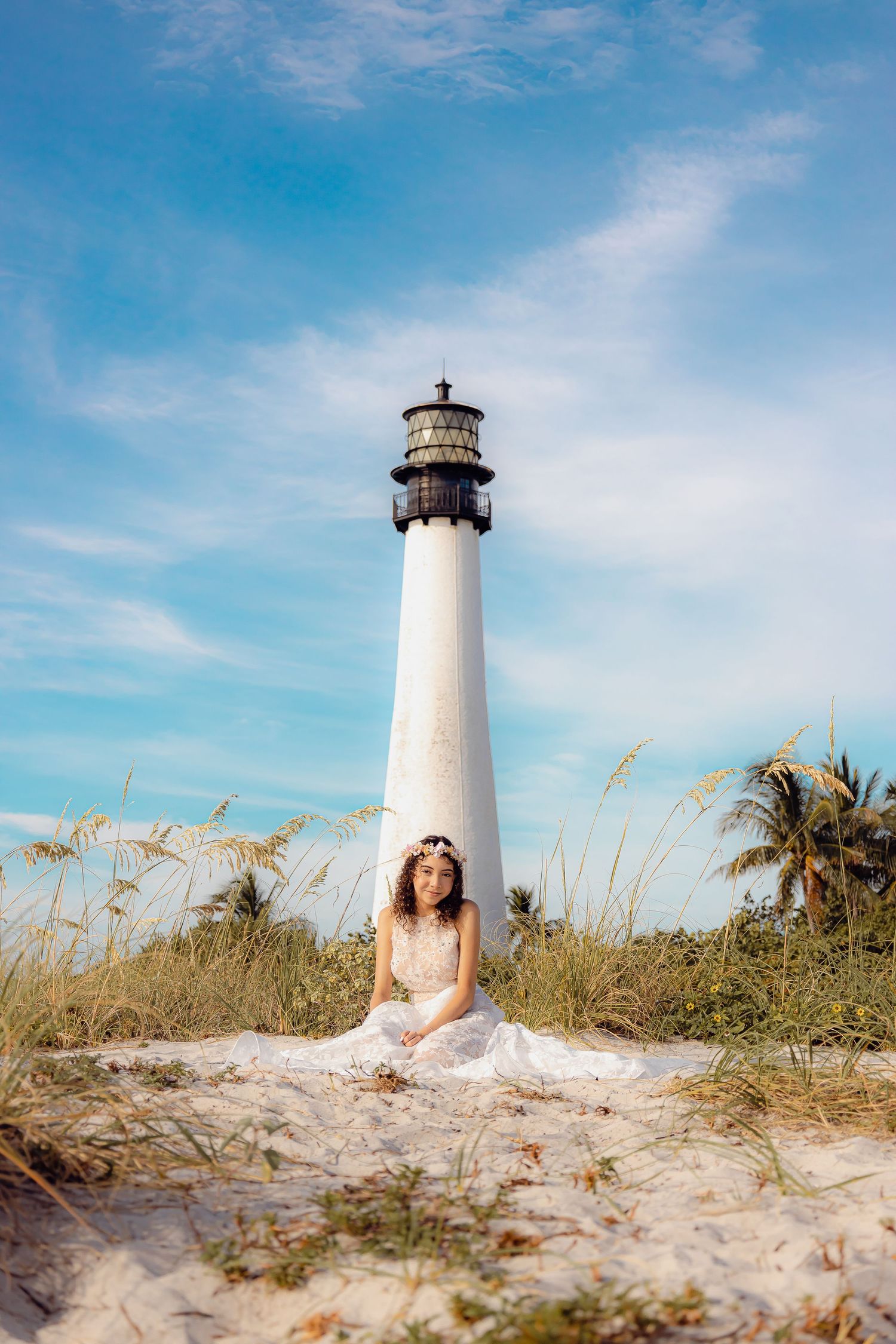 A dreamy beach portrait with a white dress against a majestic lighthouse and palm trees.