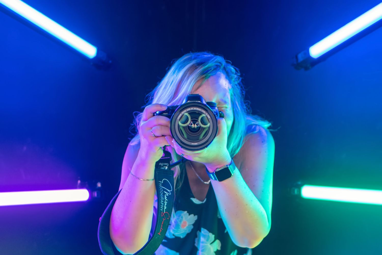 Photographer holding camera with neon lights creating colorful ambient background.