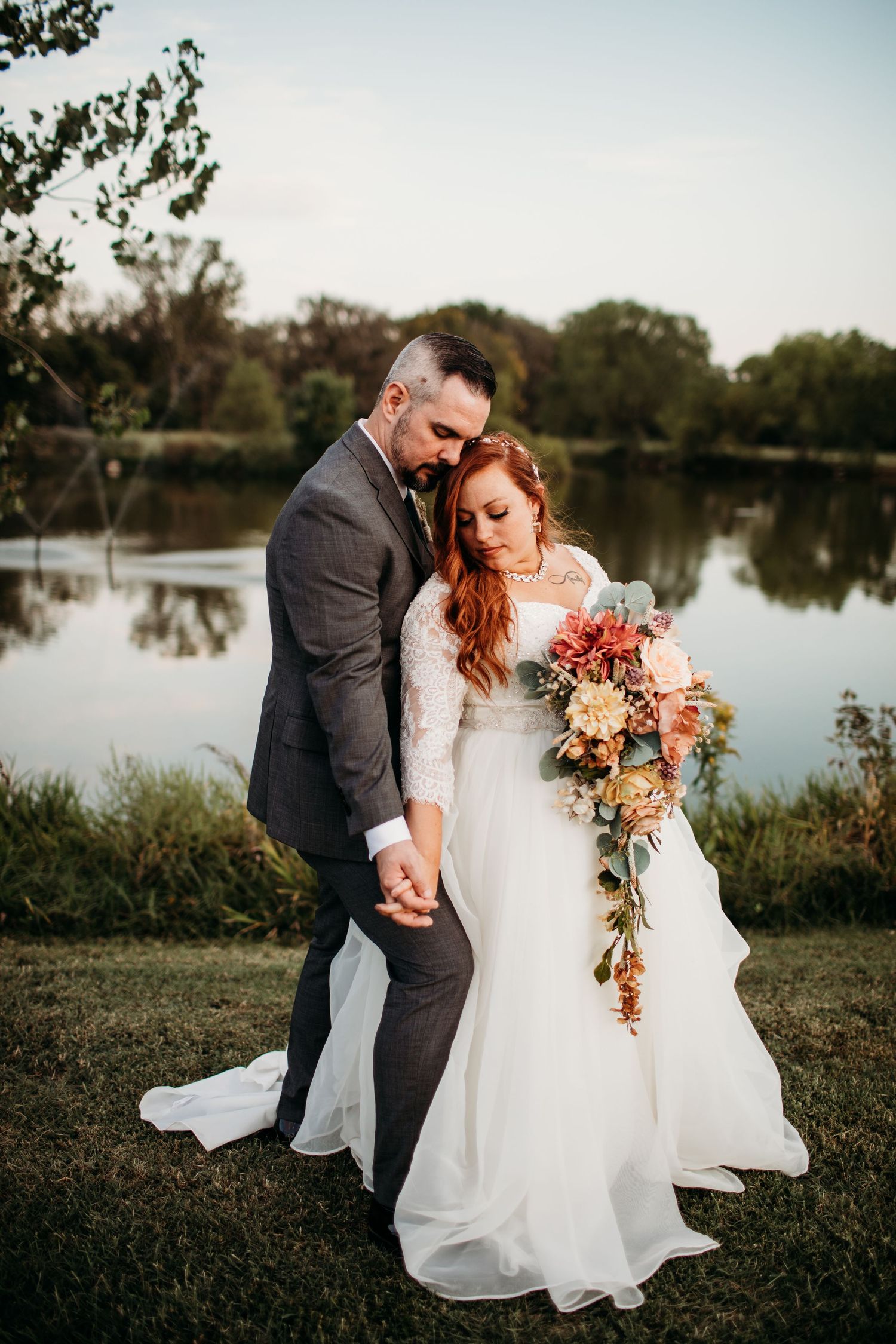 A romantic sunset wedding portrait with couple holding hands by a serene lake.