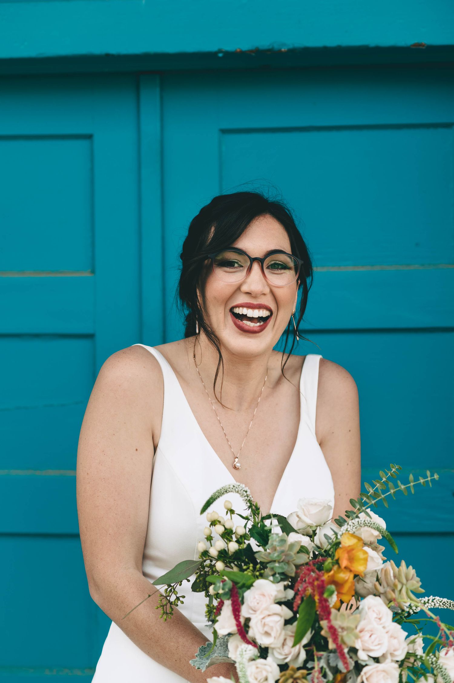 Bride with glasses having a giggle in front of blue door.
