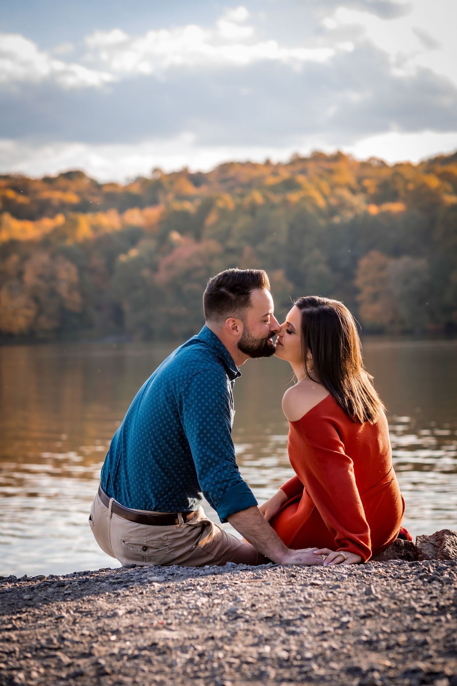 A couple sits on rocks with golden light streaming behind them. Colorful trees splatter the background
