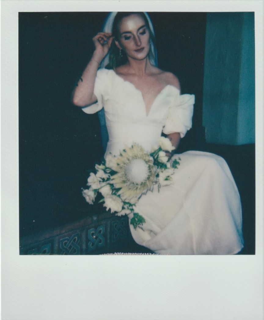 A bride in an elegant white off-shoulder gown holds a delicate bouquet.