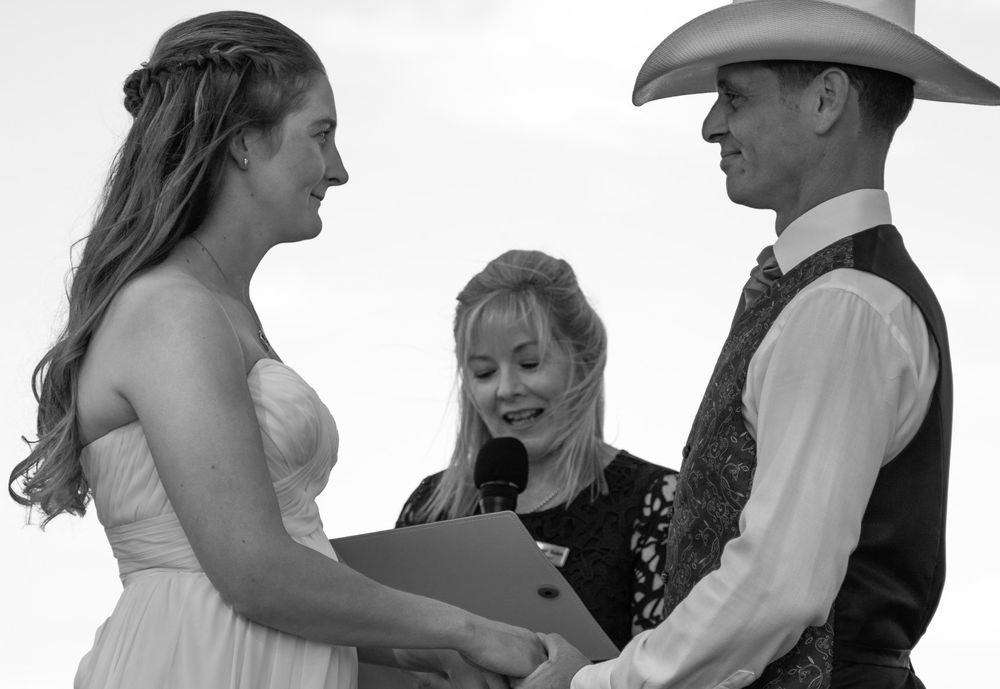 A wedding ceremony takes place outdoors with participants in western-themed attire.