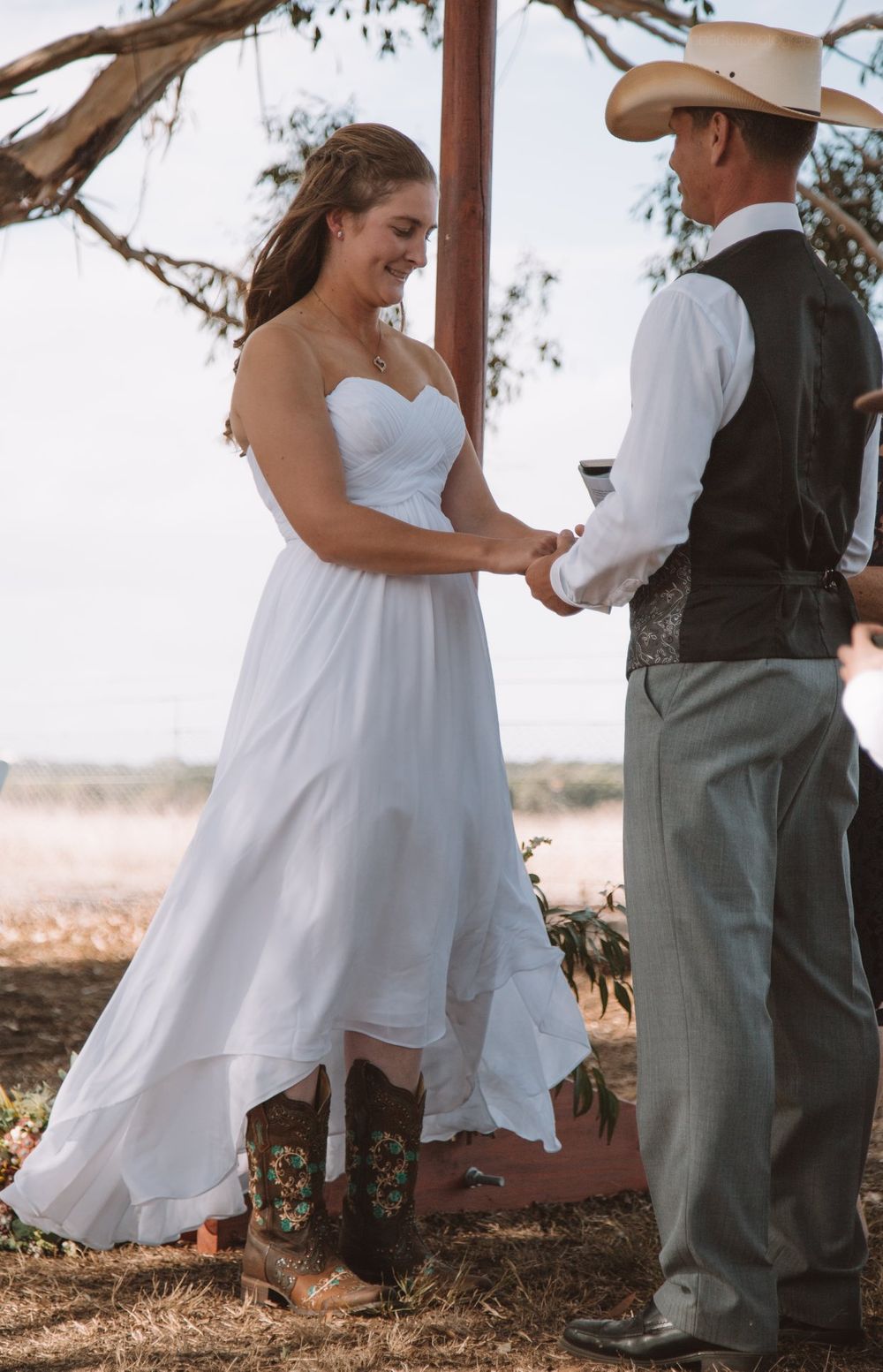 Wedding couple holding hands during outdoor ceremony under wooden arch.