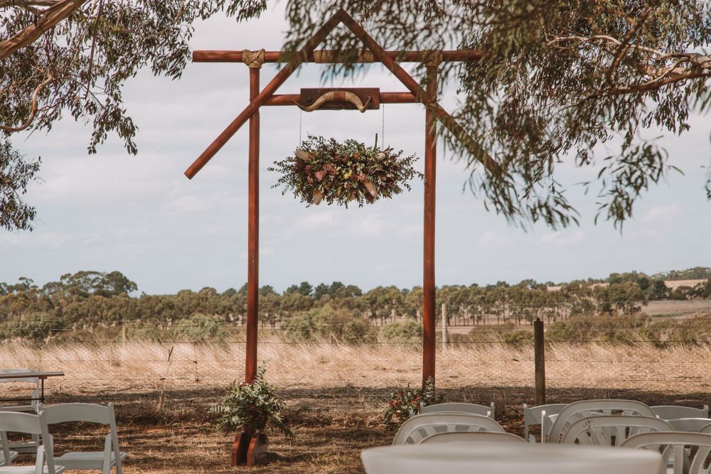 Wooden wedding arch with suspended floral arrangement in rustic outdoor setting.